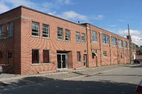 Red brick building on a city street with multiple windows and a central entrance, showcasing urban architecture and potential for redevelopment.