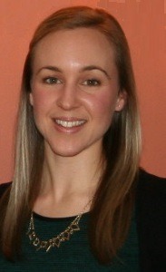 Smiling woman with long, straight hair wears a black cardigan and a statement necklace, set against a soft orange background.
