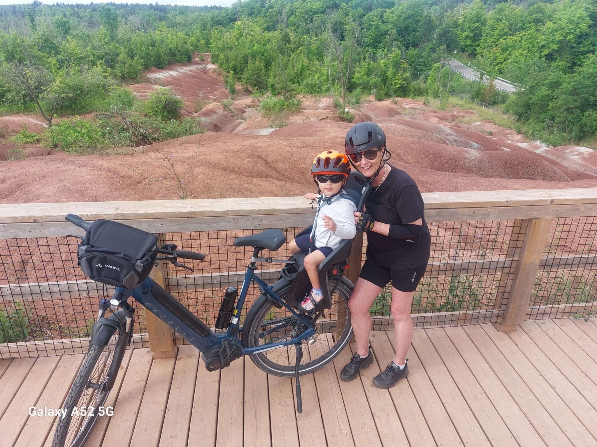 Woman and child on a bike overlook colorful, layered earth formations. The scene captures a moment of exploration and enjoyment of nature.