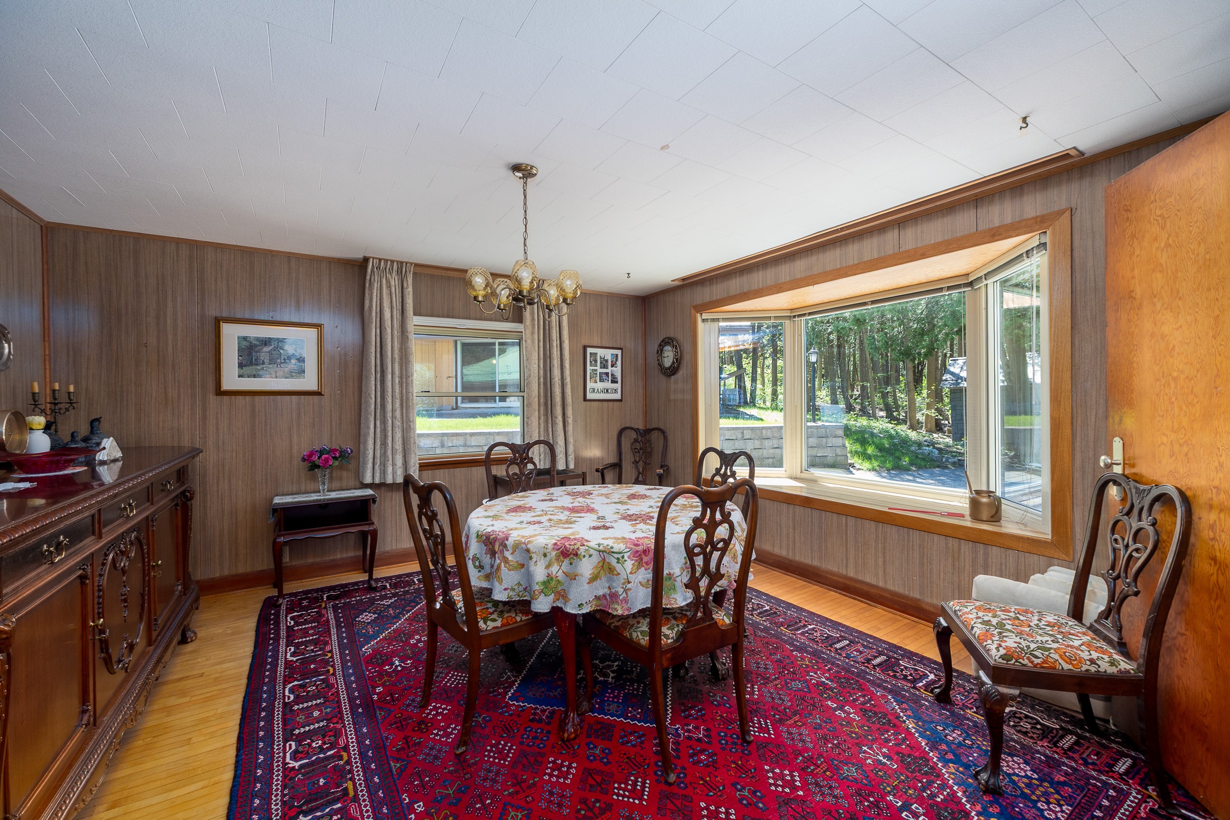 Cozy dining area featuring a round floral tablecloth, wooden chairs, and a large window with views of greenery, perfect for family gatherings.