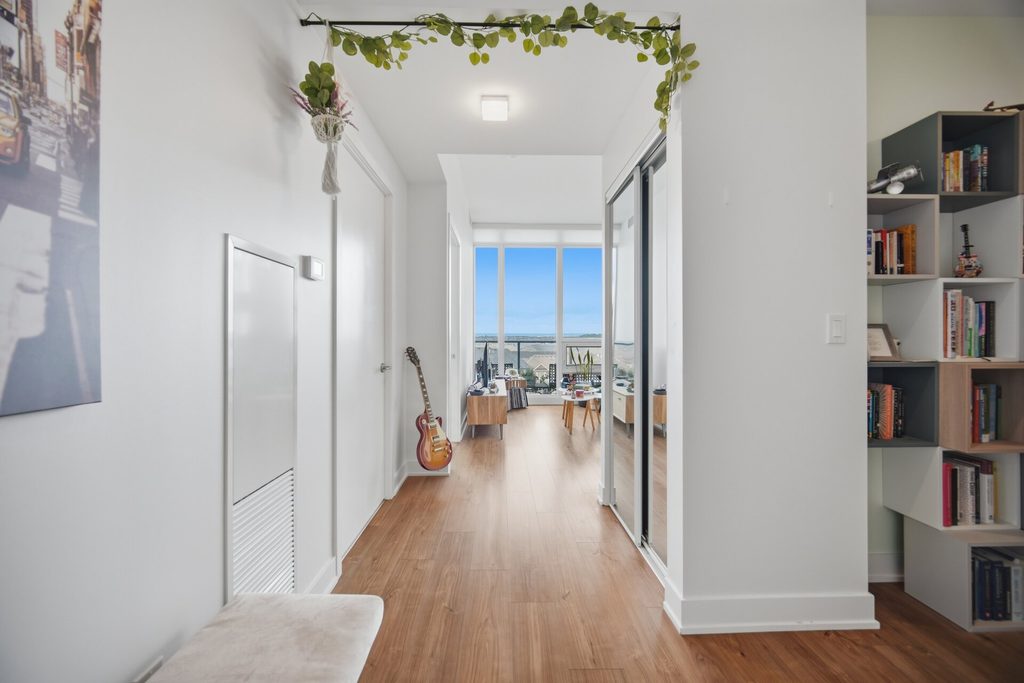Bright, modern entryway featuring a lemon-patterned doormat, a beige bench, and a wall art piece depicting a city street scene.
