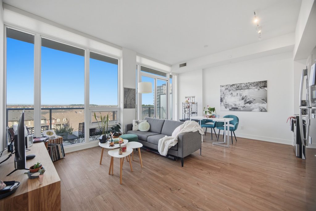 Bright hallway with wooden floors leading to a spacious room featuring large windows and views. A guitar and bookshelves add personal touches.