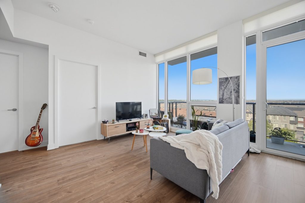 Bright and modern living room featuring large windows with a view, a gray sofa with a throw blanket, and a wooden TV stand with decor.