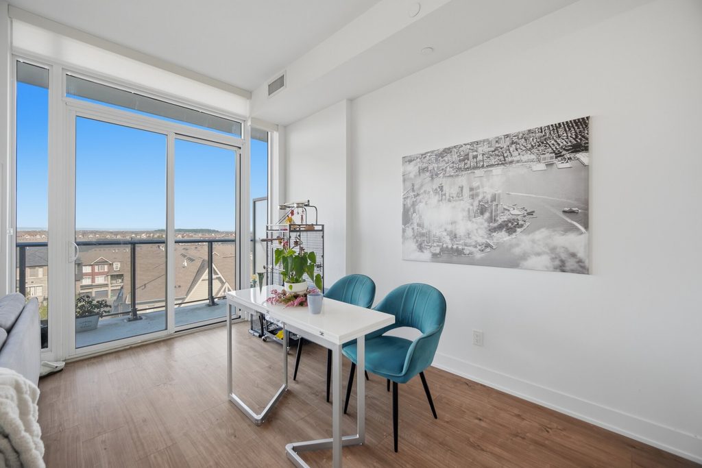 Bright, modern workspace featuring a table with teal chairs and a plant, large windows overlooking a scenic view, and a black-and-white cityscape artwork on the wall.