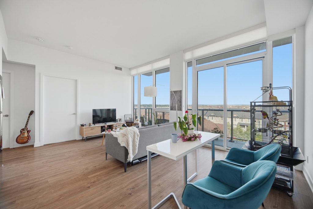 Bright, modern workspace featuring a table with teal chairs and a plant, large windows overlooking a scenic view, and a black-and-white cityscape artwork on the wall.