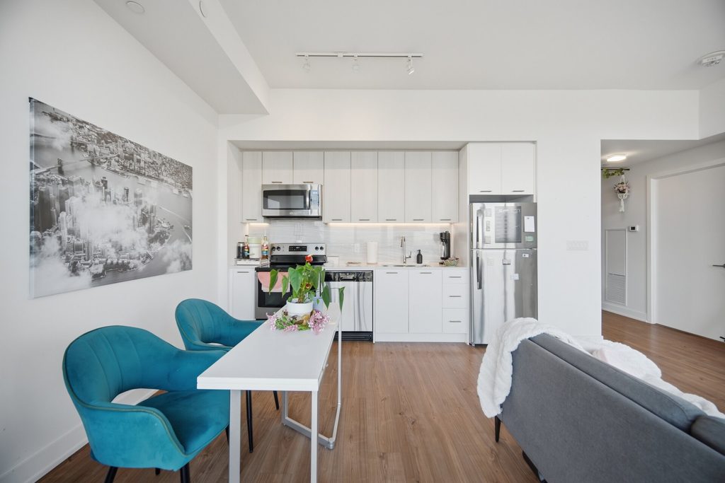 Bright, modern living room with panoramic windows, featuring a gray sofa, blue chairs, a TV, and decorative plants. Ideal for showcasing contemporary interior design.