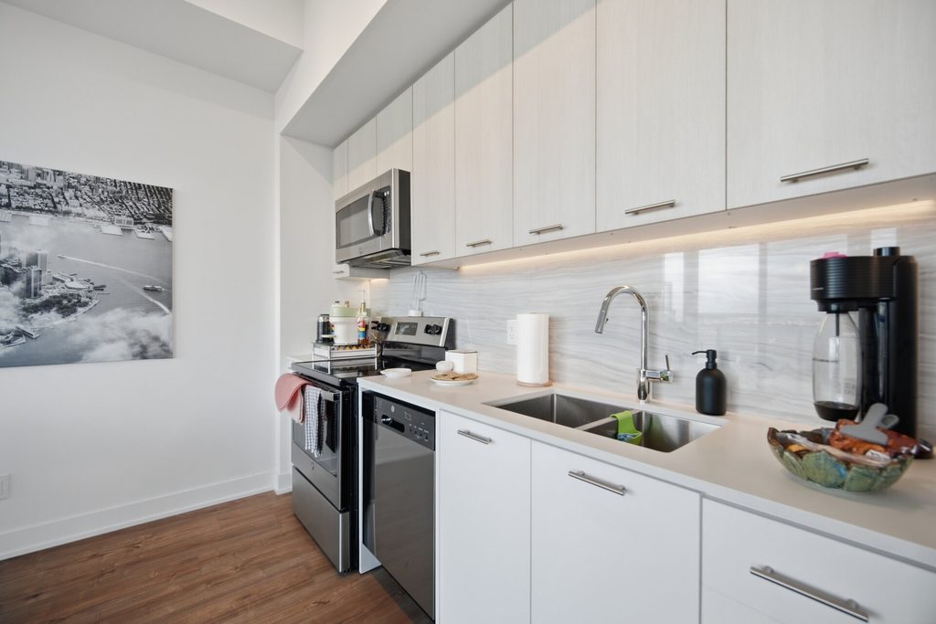 Modern kitchen with stainless steel appliances, white cabinets, and a marble backsplash. A cityscape photo adorns the wall, enhancing the aesthetic.