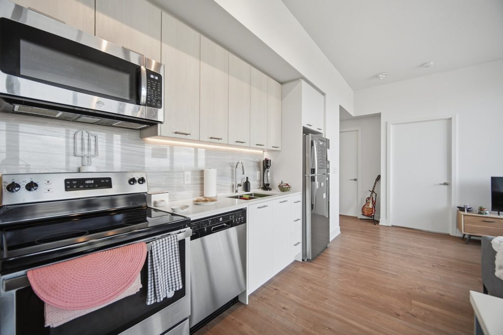 Modern kitchen featuring stainless steel appliances, white cabinetry, and wood flooring. Includes essential cookware and a glimpse of adjacent living space.