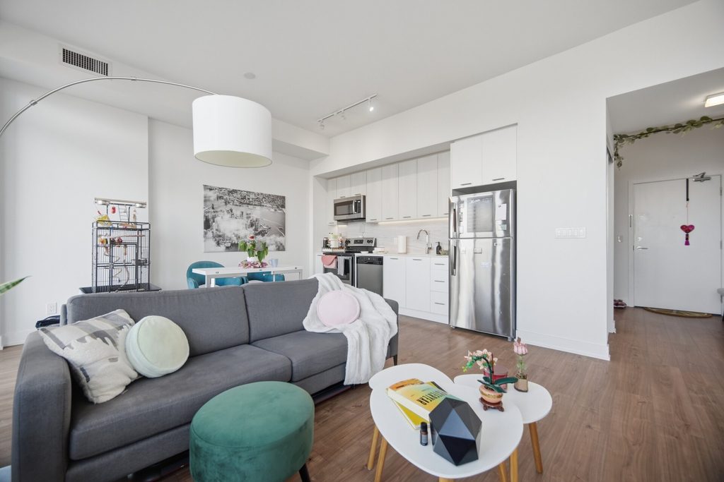 Modern living room showcasing a cozy gray sofa with colorful pillows, a sleek kitchen, and a dining area with vibrant decor, emphasizing stylish interior design.