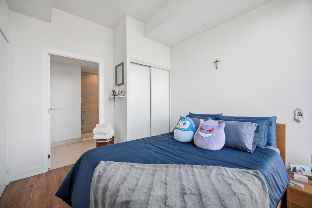 Bright bedroom featuring a blue bedspread and plush toys, with large windows showcasing a clear outdoor view. Ideal for showcasing modern interior design.