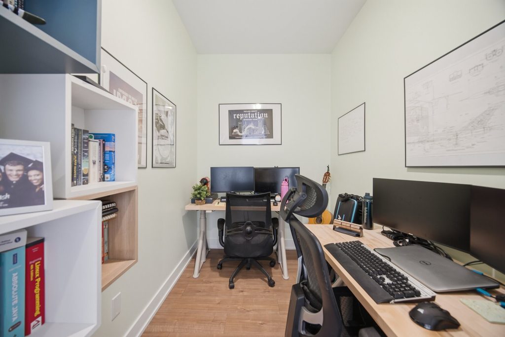 Cozy home office with dual computer setup, bookshelves, and framed artwork. Ideal for productivity and remote work.
