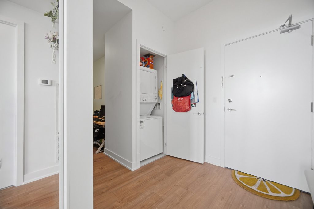 Entryway showcasing a clean, modern space with a stacked washer and dryer in a closet on the left, and a welcoming floor mat by the door.