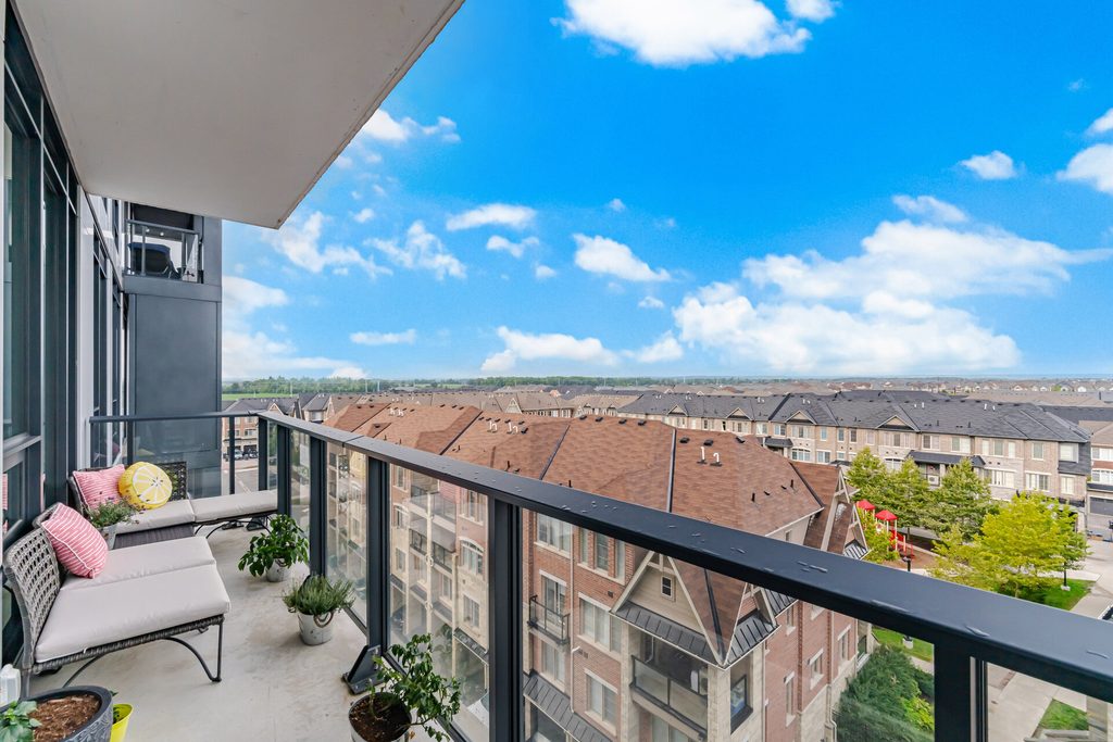 Modern balcony with seating and potted plants, offering a panoramic view of neighboring rooftops and a clear sky, enhancing outdoor living appeal.