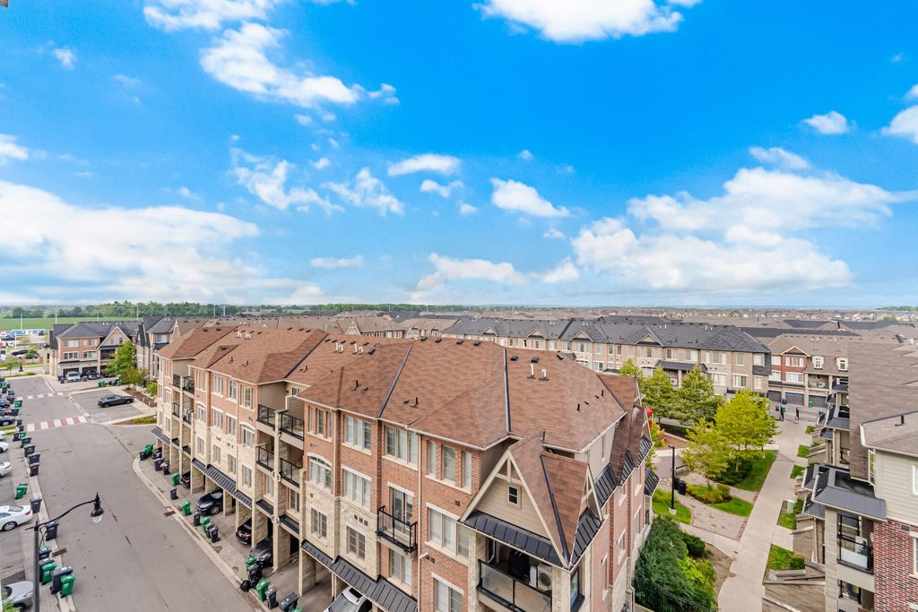 Aerial view of a residential neighborhood featuring modern townhouses with brown roofs, well-maintained streets, and green landscaping under a blue sky.